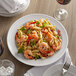 A Tuxton Concentrix white china plate with pasta, shrimp, and vegetables on a table.