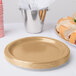 A Creative Converting glittering gold paper plate with a gold rim next to a sandwich on a stack of paper plates.