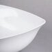 A close-up of a white Carlisle flared melamine bowl with a curved edge.
