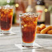 A clear 14 oz. mixing glass filled with iced soda, shown on a table with a white napkin.