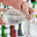 A person is pouring liquid from a decorative, cut-glass decanter into a glass filled with ice.