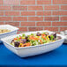 Two white Tablecraft cast aluminum salad bowls filled with salad and vegetables on a table in a salad bar.
