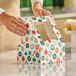 A person is assembling a festive bakery box with a holiday ornament pattern and a clear window on top.