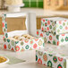 A festive bakery box with a holiday ornament print, partially open to reveal powdered donuts inside, sits on a countertop with similar closed boxes nearby.