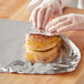 A person wearing gloves uses Choice aluminum foil to wrap a sandwich.