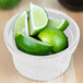A Tablecraft white cast aluminum souffle bowl filled with limes and lime slices.