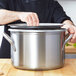 A person using a Vollrath stainless steel pot lid on a silver pot.