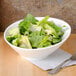 A CAC Bone White porcelain salad bowl filled with salad on a table with a fork on a napkin.