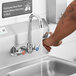 A person washing their hands at a wall mount handsink faucet with a gooseneck spout using wrist handles.