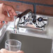 A person's hand filling a glass from a Regency wall mount bar sink faucet.