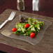 A Fineline clear plastic square plate with a salad on it.