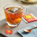 A glass cup of oolong tea with a tea bag in it on a table with a spoon and a packet of oolong tea bags.