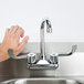 A hand with a metal object attached to a wrist reaching for the gooseneck faucet of an Eagle Group hand sink.