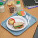 A Carlisle slate blue fast food tray with a sandwich, apple, and a drink.