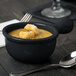 A Tablecraft black cast aluminum soup bowl with a handle filled with soup and croutons with a spoon on the table.