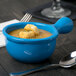 A blue Tablecraft cast aluminum soup bowl with a handle filled with soup and croutons with a spoon next to it.
