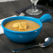 A Tablecraft sky blue cast aluminum soup bowl with soup and a spoon in it.