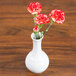 A CAC white porcelain bud vase with three red carnations on a wood surface.
