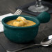 A Tablecraft hunter green cast aluminum soup bowl with a spoon and fork on a table.