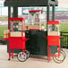 A red Carnival King commercial popcorn machine on a cart with a red umbrella.