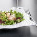 A plate of salad with chicken and vegetables on a white square melamine bowl.
