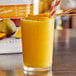 A glass of Torani Mango Fruit Smoothie Mix with a straw and orange slices.