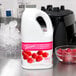 A white jug of Torani Raspberry Fruit Smoothie Mix next to a bowl of raspberries.
