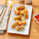 A rectangular white Acopa porcelain platter with fried spring rolls.
