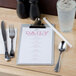 A Menu Solutions Alumitique clipboard holding a menu on a table next to silverware.