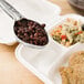 A Vollrath ivory perforated oval spoodle spoon serving beans and pasta on a tray.