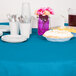 A blue table with turquoise table cover, plates, and cups of utensils.
