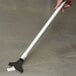 A person holding a silver and black Unger floor scraper with a metal pole handle.