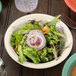 A bowl of salad with onions and carrots in a GET Diamond Ivory melamine bowl.