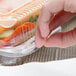A hand holding a Durable Packaging clear hinged plastic container with a sandwich inside.