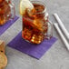 A glass mug with a Choice Purple beverage napkin and a lemon slice on the rim on a table with a glass jar of ice.