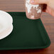 A hand holding a paper cup over a Cambro Sherwood Green rectangular tray.