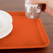 A hand holding a paper cup over a Cambro rectangular orange tray.
