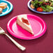 A slice of cheesecake on a Creative Converting hot magenta pink paper plate with a fork.