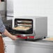 A person in an apron putting trays of food into an Avantco countertop convection oven.