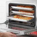 A person taking pizza out of a Avantco countertop convection oven.