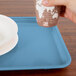 A person holding a cup over a blue Cambro cafeteria tray.