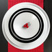 A white Elite Global Solutions round melamine plate with a black and red swirl design holding raspberries.