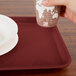 A hand holding a paper cup over a Cambro tray on a table.