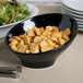 A black slanted melamine bowl filled with croutons next to a salad.