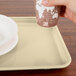 A hand holding a cup over a Cambro tray with a plate on it.