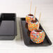 A black Elite Global Solutions rectangular melamine tray with candy apples on it.