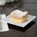 A white GET Siciliano square plate with a piece of cake on it.