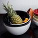 A black Elite Global Solutions melamine bowl with fruit inside.