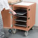 A person putting trays in a Cambro mobile cart.
