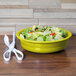 A Fiesta Lemongrass China bowl filled with salad next to a pair of scissors on a table.